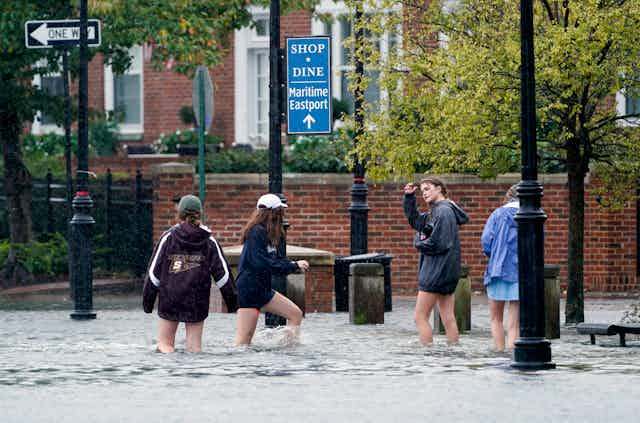 Teens walk through knee-deep water on a sidewalk