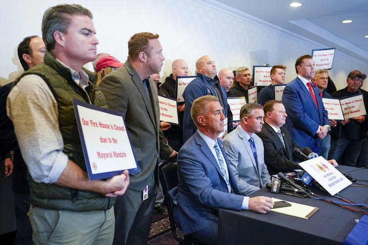 New York firefighters hold signs opposing vaccine mandates during a news conference.