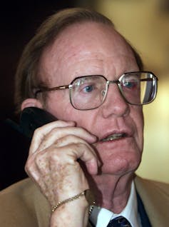 A man wearing glasses speaks into a large cellphone.