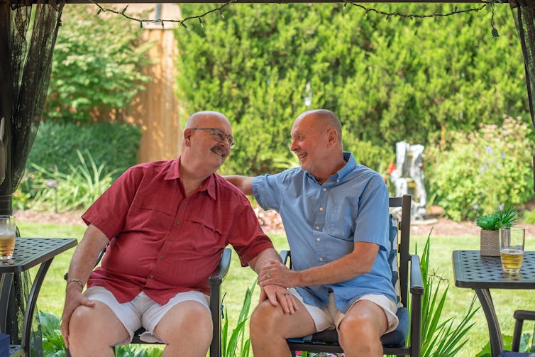 An older same sex couple laugh together in the garden.