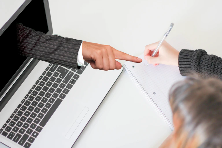 Accusing finger pointing out of laptop screen at woman writing