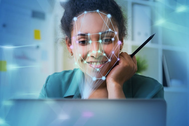 Young African American woman looking at laptop with facial recognition mapping superimposed on her face