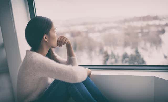 Woman sits by the window, looking out longingly
