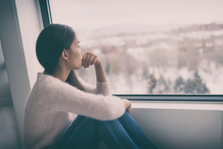 Woman sits by the window, looking out longingly