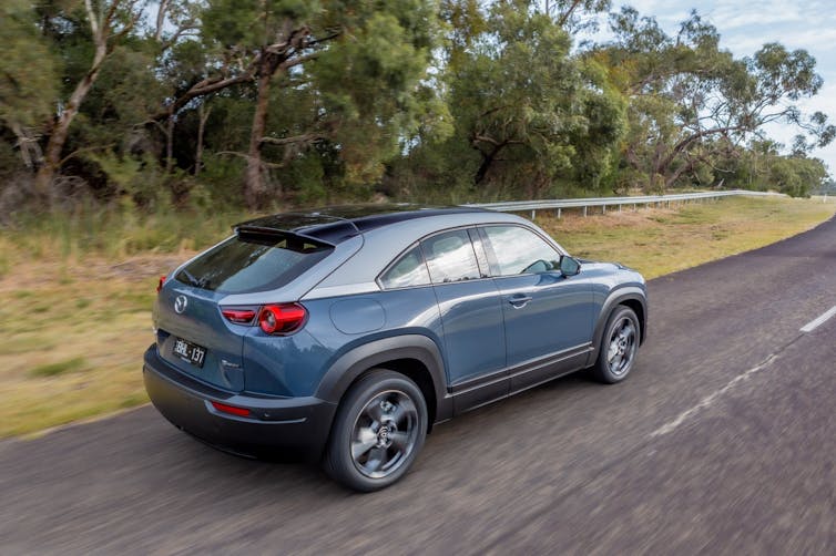 Blue electric car drives on bush-lined road