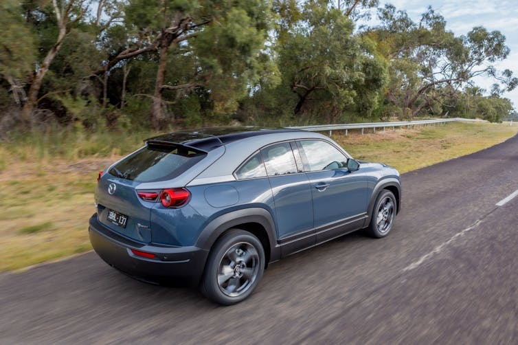 Blue electric car drives on bush-lined road
