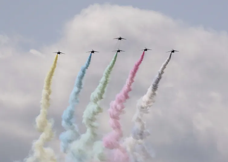 Six fighter planes from the Japan Air Self-Defense Force (JASDF) give an aerobatic display, with vapour trails depicting the colours of the Olympic rings.