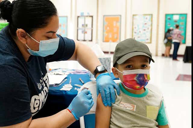 Un jeune garçon, portant une casquette et un masque, reçoit une dose de vaccin d'une infirmière.