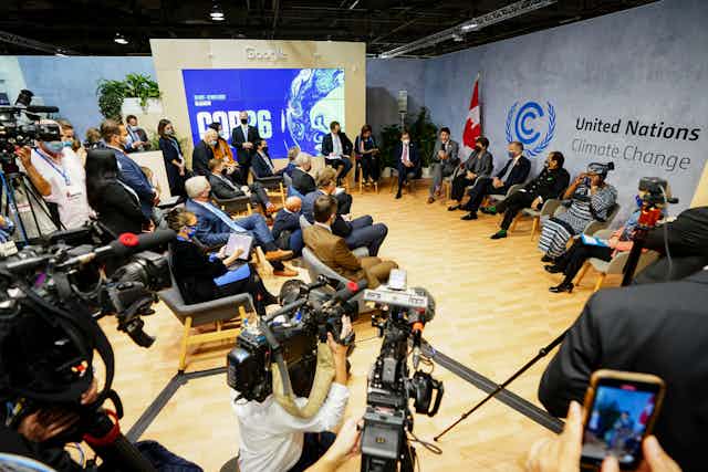 Media aim their cameras and reporters sit in chairs before a panel of leaders and experts on carbon pricing, in front of a banner reading United Nations Climate Change.