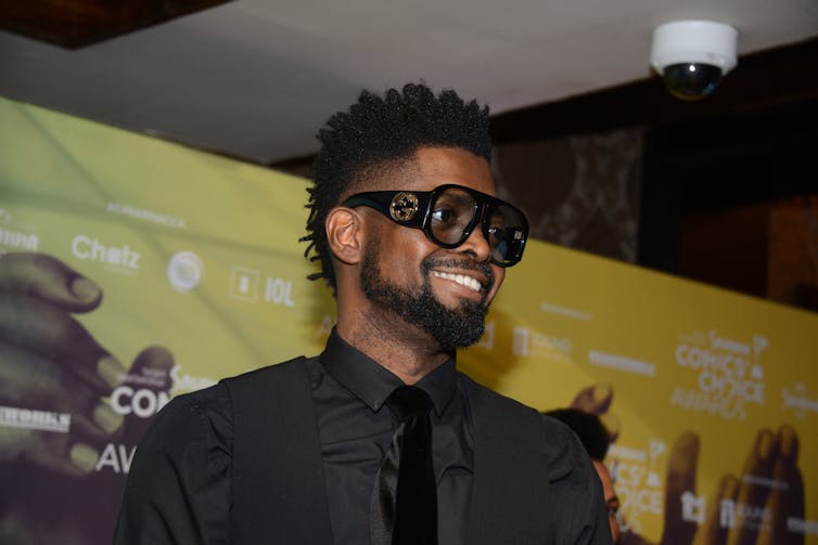 A man with shaggy hair and designer shades smiling.