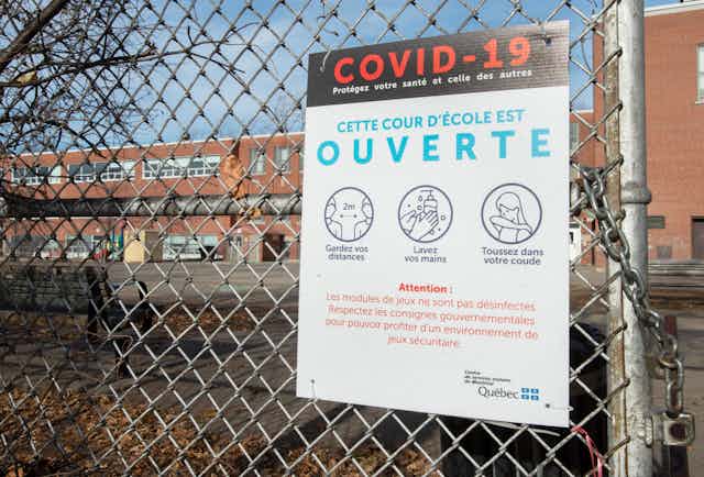 A COVID-19 precautions sign is seen affixed to a schoolyard fence.