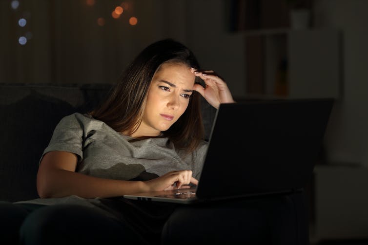 A young woman is seen squinting at a laptop.