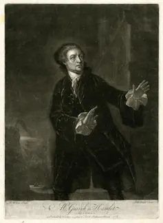 A man standing with hands outstretched and a grey castle background.