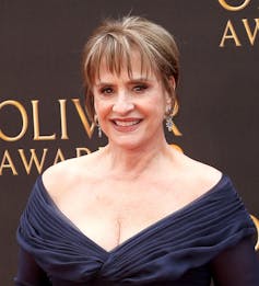 An actress in dangly earrings and a wide-necked dress showing her decolletage.
