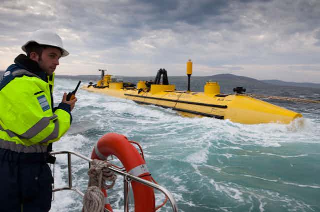A worker in high-visibility jacket looks on at a yellow floating structure.