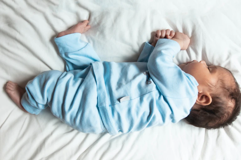 A small baby sleeps on their side wearing blue pajamas on a white sheet