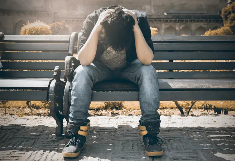 Un jeune est assis, triste, sur un banc