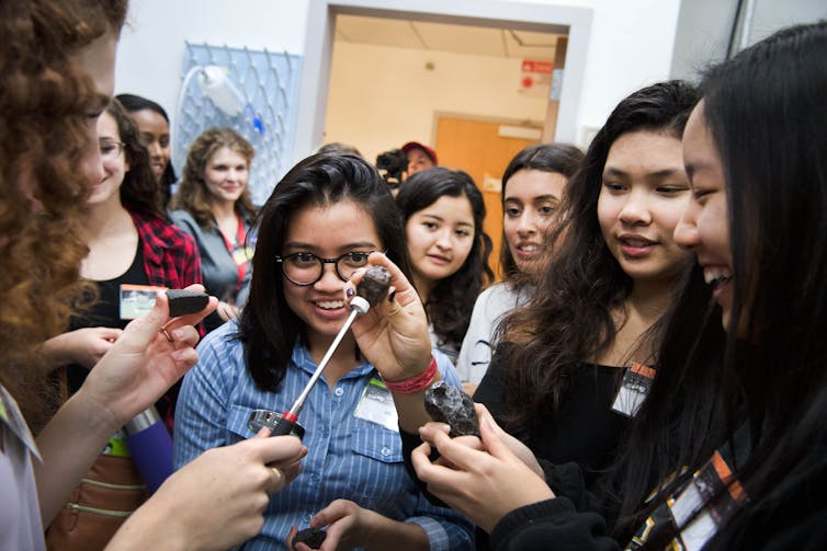 People gather around someone holding a scientific instrument