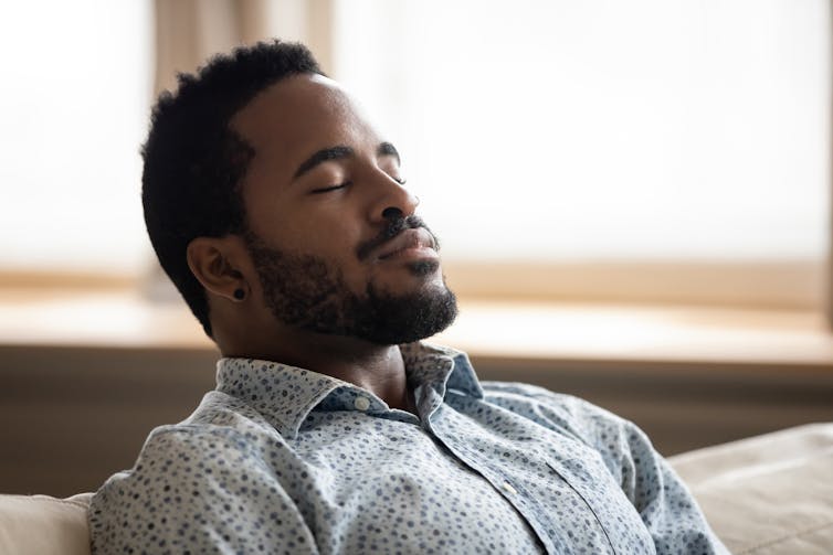 A man is sitting on a couch with his head leaned back against the sofa.