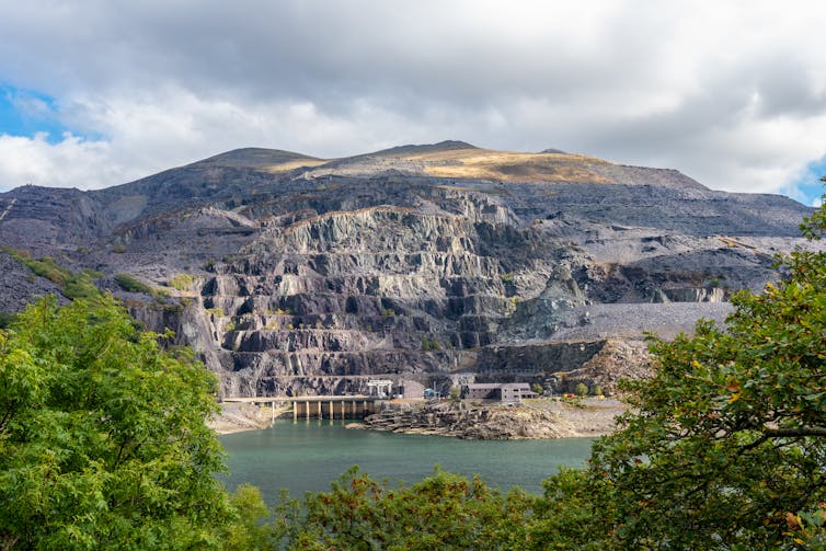 Old quarried mountain viewed across a lake with buildings at base