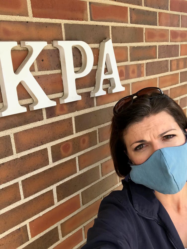 Emily Bradbury, Kansas Press Association head, stands in front of a building with the Kansas Press Association logo. on it.