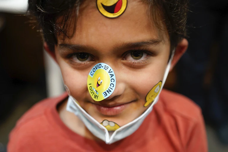 enfant qui sourit en montrant les autocollants sur son visage après avoir été vacciné contre la COVID-19.