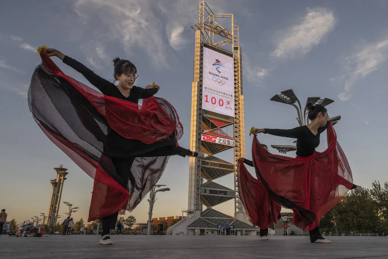 Women in red and black outfits rehearsing a dance in front of an Olympic sign in Beijing, China
