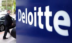 A pedestrian walks past a blue and white Deloitte sign.