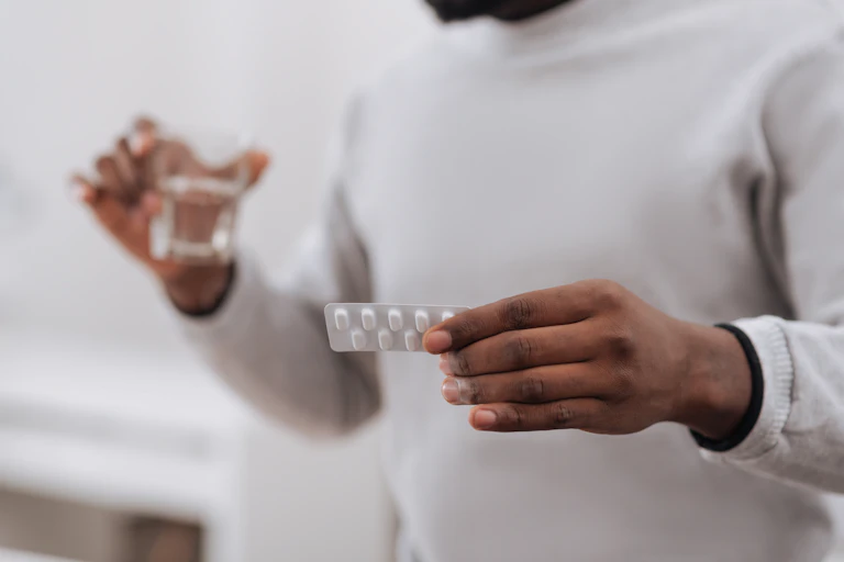 Man holding blister pack of medication in one hand and a glass of water in the other.