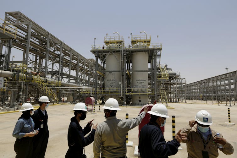 Engineers and journalists look an industrial site with containing pipelines and gas storage containers