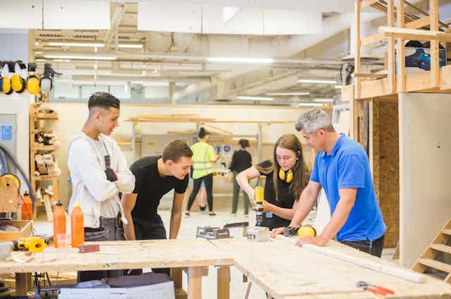 A group of students and a teacher work together in a wood shop building lab.