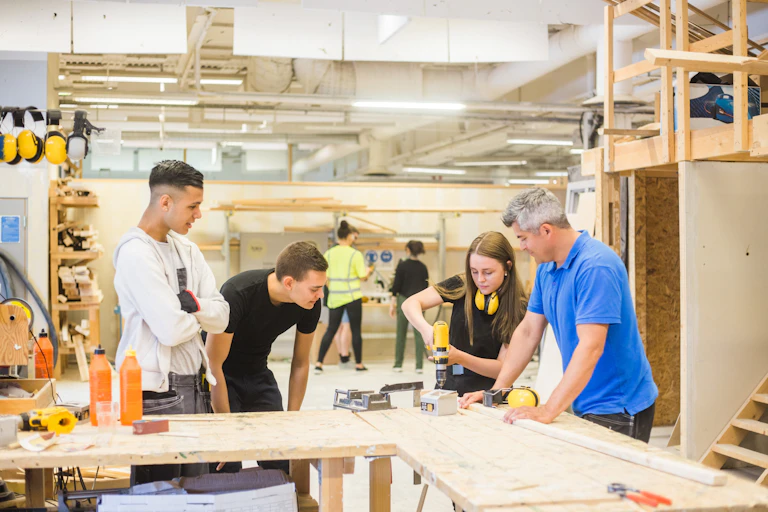 A group of students and a teacher work together in a wood shop building lab.