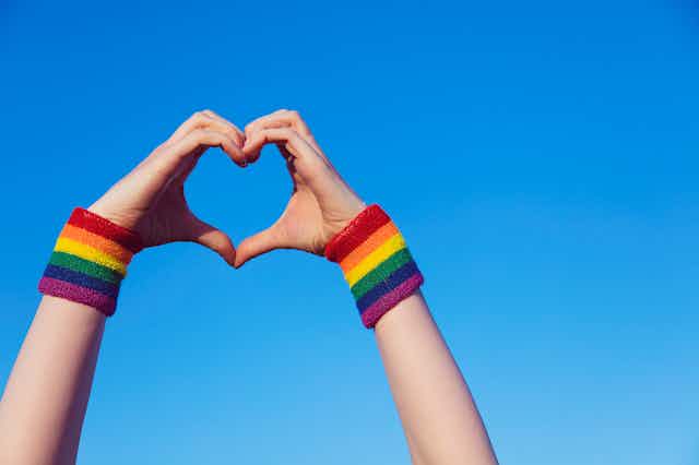 Two hands in the shape of a heart with rainbow bracelets at the wrists. 