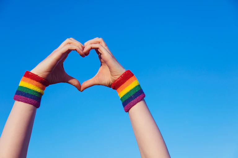 Two hands in the shape of a heart with rainbow bracelets at the wrists.