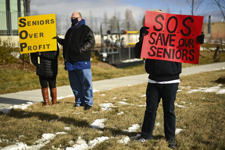 People protest outside a long-term care home, one carrying a sign that reads Save our Seniors and another carrying a sign that reads Seniors Over Profit