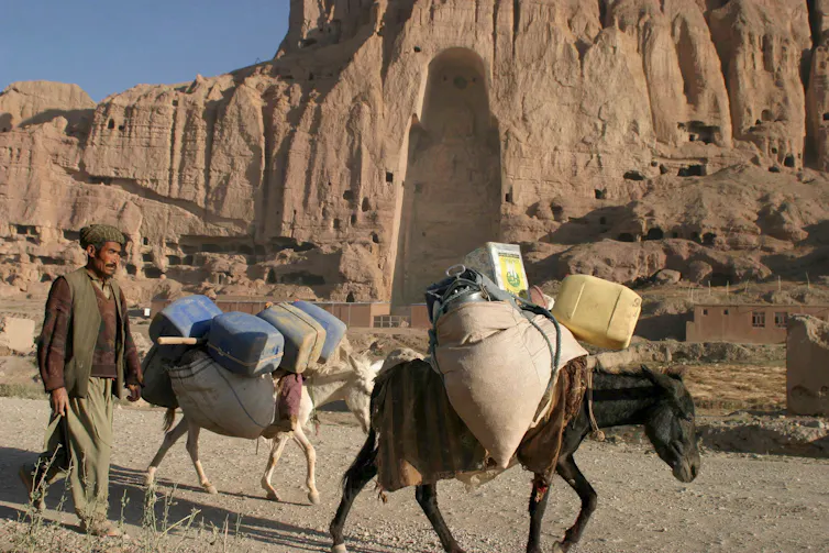 A man and two donkeys walk by cliff-face with a figure-shaped cave carved out