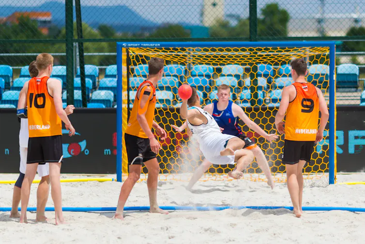 Des hommes portant des vêtements oranges jouent au volleyball de plage
