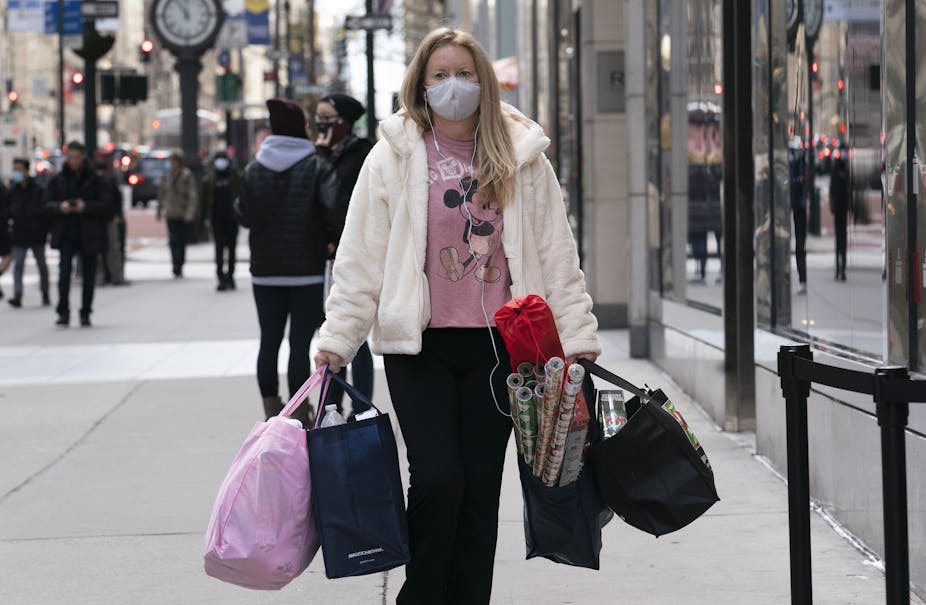 a woman wearing a mask carries four shopping bags stuff with stuff on the sidewalk in New York. 
