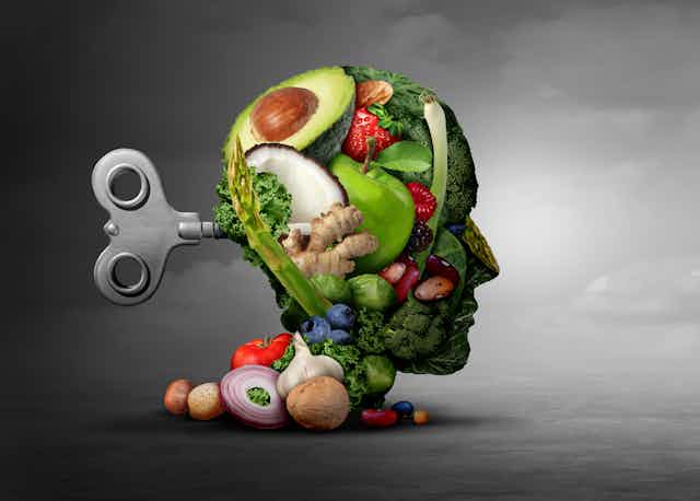 Illustration of a human head made out of fruit and vegetables with a wind-up key in the back, against a grey cloudy background