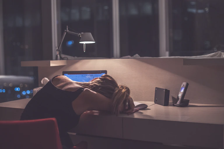 Exhausted female student falls asleep at desk while studying at night