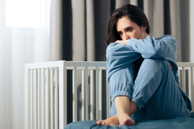 Woman in pyjamas sitting near cot looking depressed