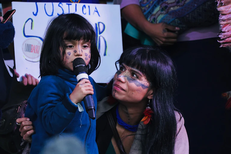 young girl talks into microphone as mother watches on