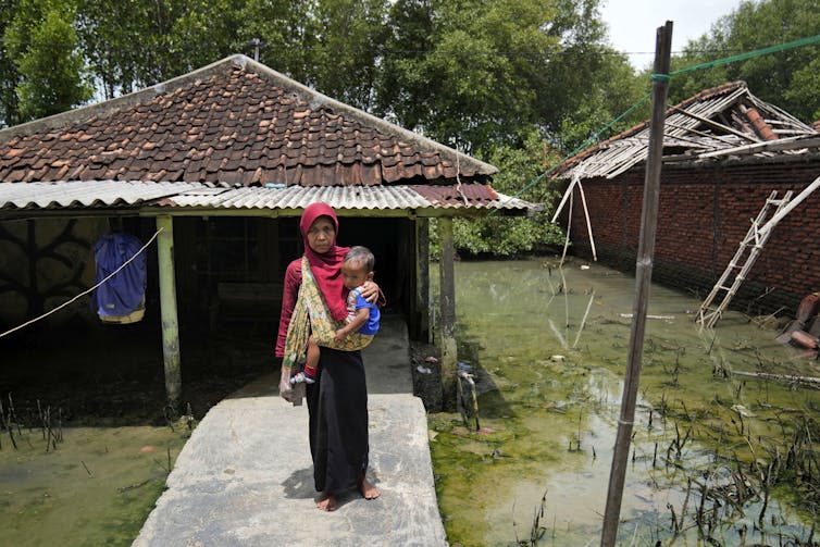 woman holds child outside home surrounded by water