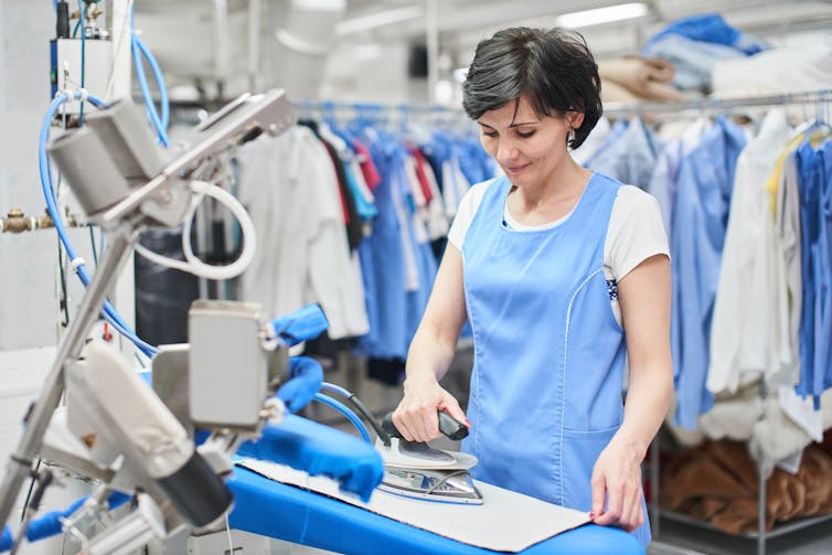A woman in a blue apron ironing in an industrial laundry
