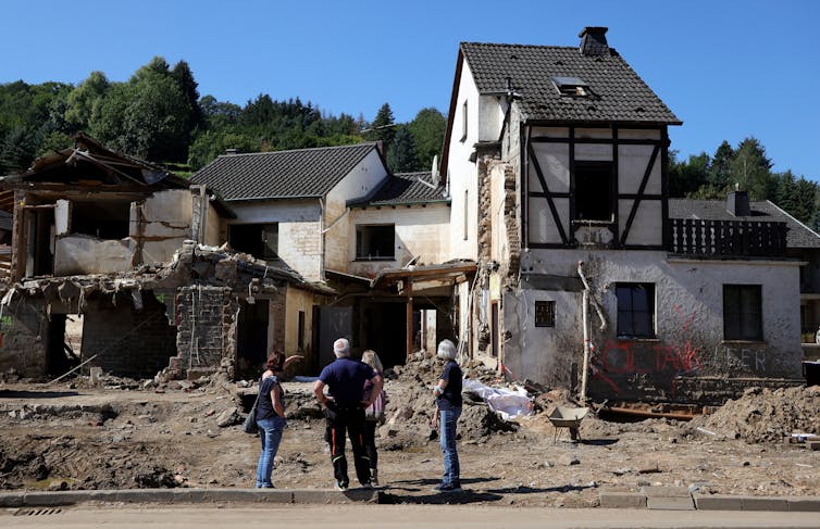 Four people looking at a German home with severe flood damage.