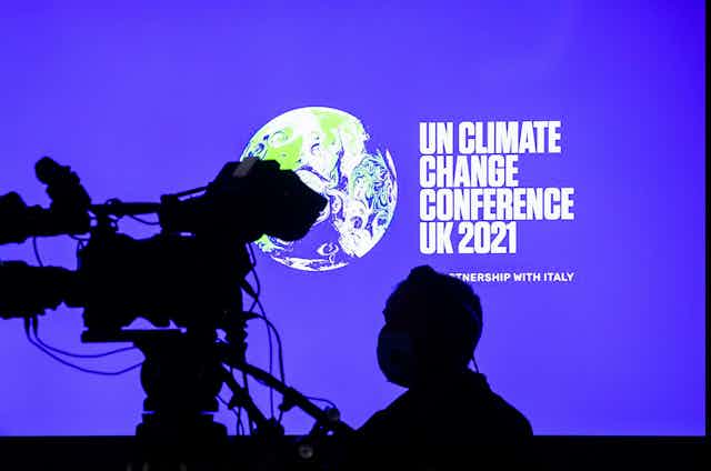 Cameraman stands in front of COP26 screen