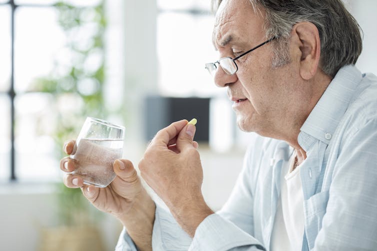 An elderly man taking a pill with a glass of water