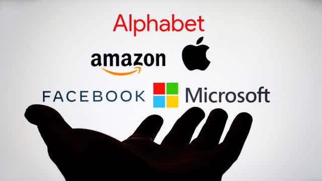 A group of the big tech company names above a hand in shadow.