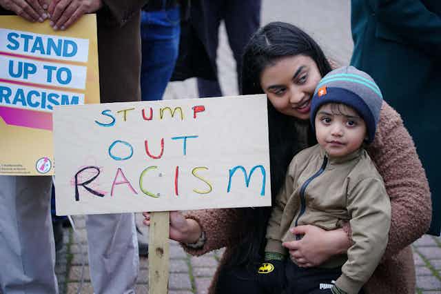 An British Asian woman with a small child holding a banner reading: 'Stump Out Racism' during a protest outside Yorkshire County Cricket Club's Headingley Stadium in Leeds, November 2021.