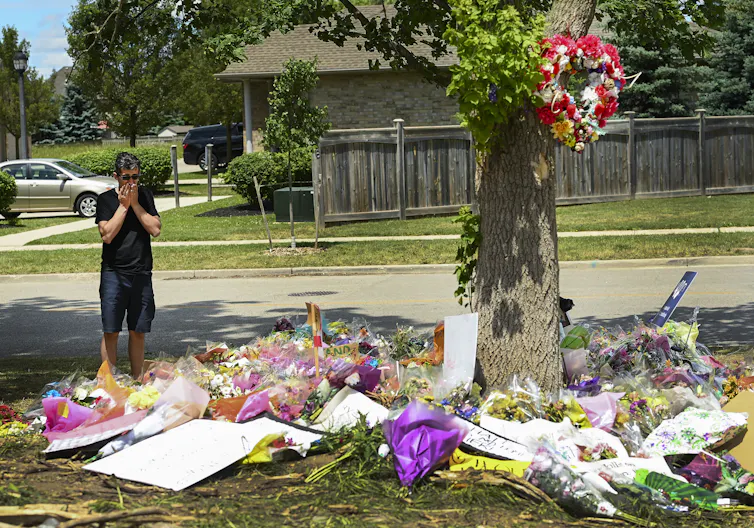 A man with his face stands near tribute featuring flowers and signs.